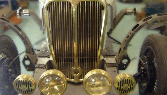 A restored vintage car's grill showcases the chrome & brass trim on the grill and headlights at Upper Classics NZ workshop
